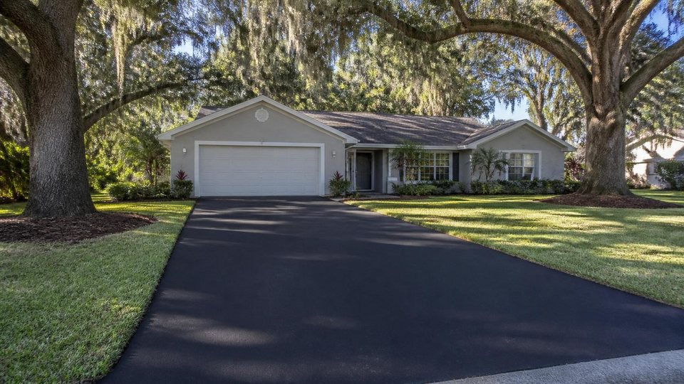 Freshly paved black asphalt driveway leading to a single-storey Florida home under live oaks